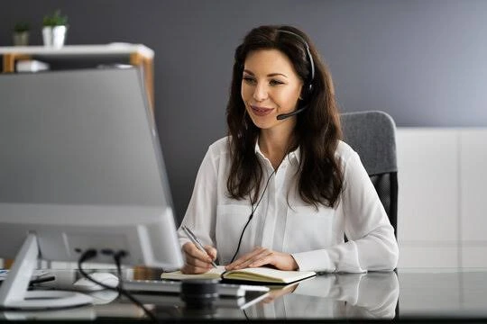 Office professional wearing a headset taking notes at a desk, representing dedicated offshore support staff